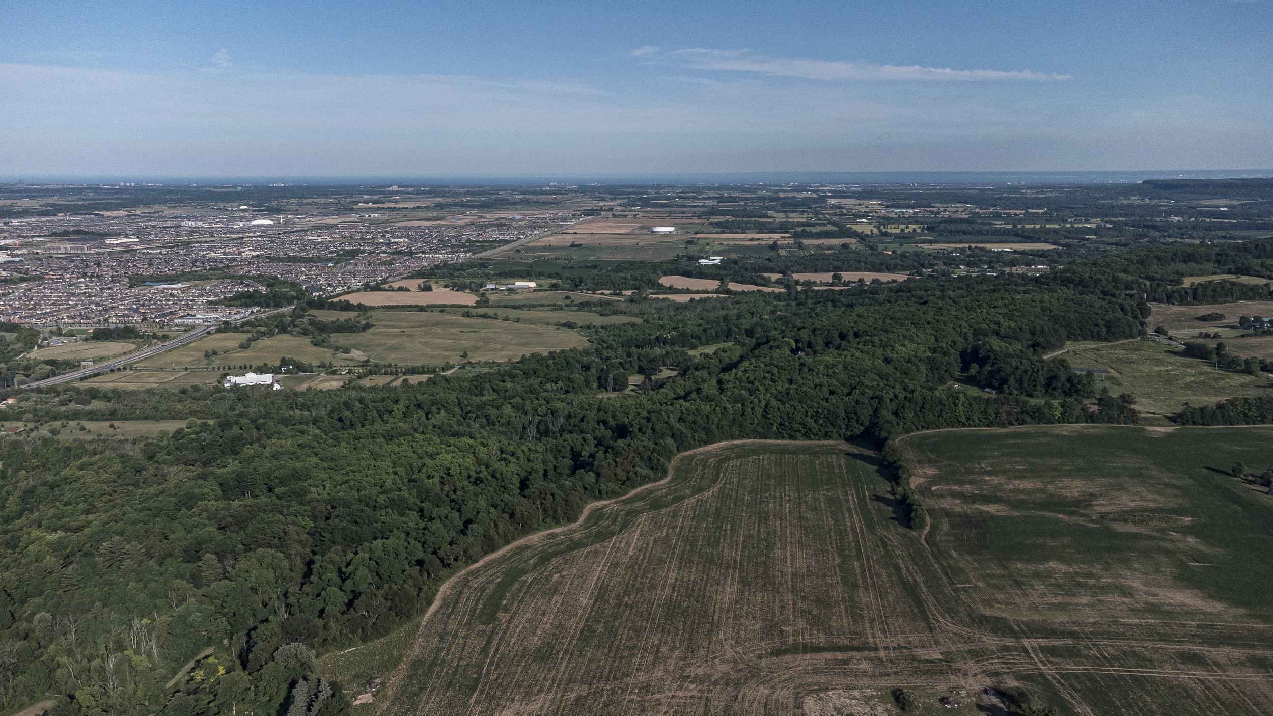An aerial view of farmland, a road and subdivisions on a sunny day