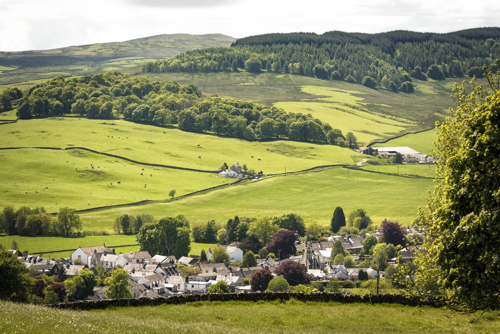 photo of a small village surrounded by green fields lines with trees and hedgerows